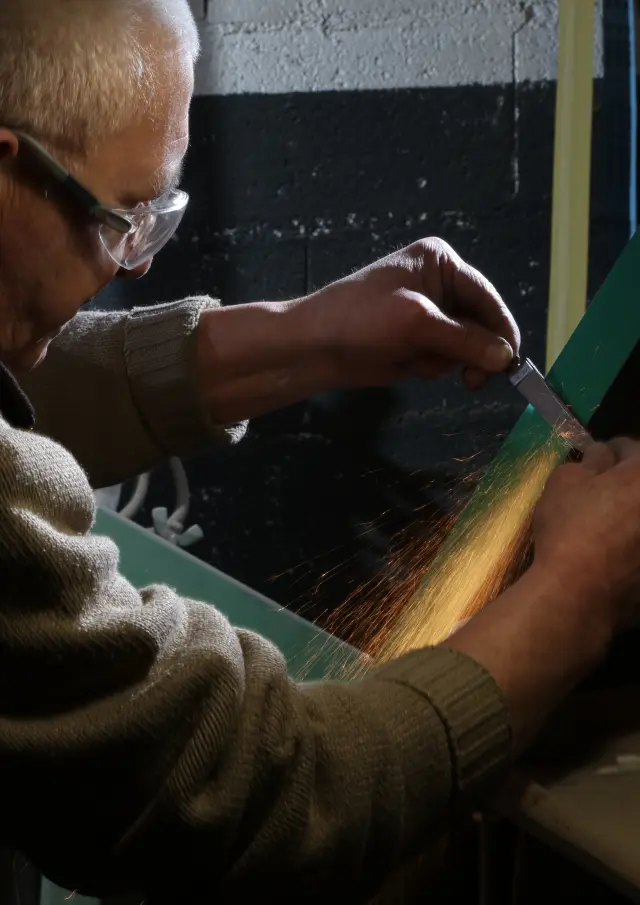 Artisan de la coutellerie Robert David affûte une lame de couteau sur machine à Thiers
