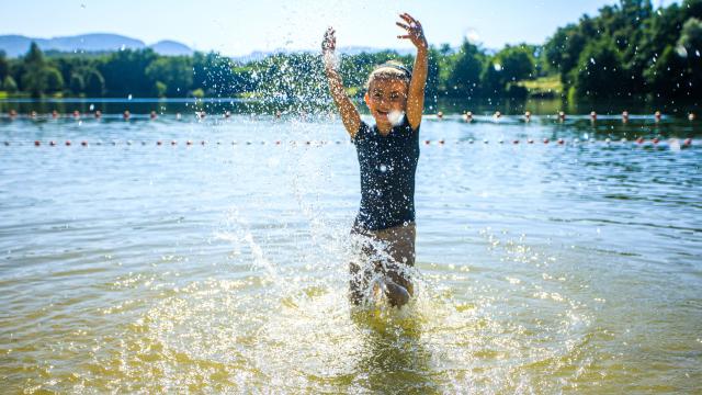 Une fillette dans le plan d'eau d'Iloa éclabousse l'objectif de la caméra par une belle journée ensoleillée, avec des arbres visibles au loin.