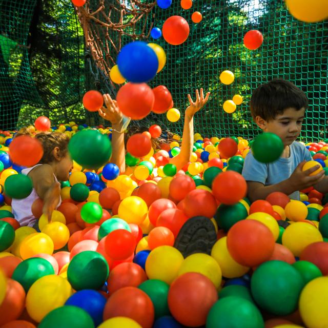 Trois enfants jouent dans un filet à Prabouré, entourés de boules colorées, avec des arbres en arrière-plan.