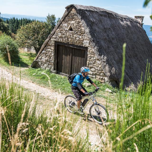 Cycliste en VTT devant une jasserie sur les crêtes du Forez, entouré de végétation et d’un paysage dégagé.