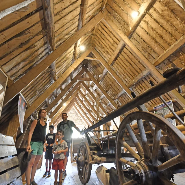 Famille visitant l'espace muséographique de la jasserie du Coq Noir à Saint Anthème, sous le toit.