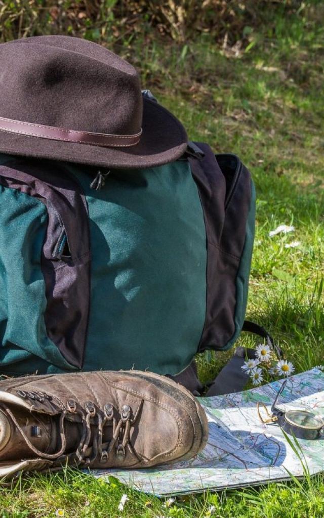 Équipement de randonnée comprenant un sac à dos, des chaussures, une carte et une boussole, posé sur une pelouse fleurie.