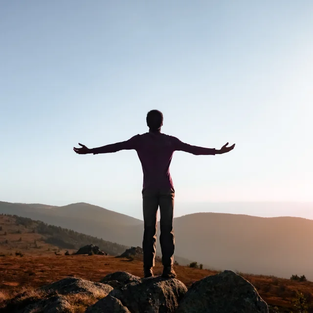 Un randonneur, à Peyre Mayou, face à l’horizon, bras ouverts, contemple les vastes paysages du Livradois-Forez au lever du soleil. Capturée en Auvergne, cette image évoque la liberté, l’évasion et le ressourcement au cœur de la nature. Parfaite illustration d’un séjour bien-être, d’une escapade randonnée ou d’une expérience de déconnexion totale en montagne. Ciel dégagé, lumière dorée et panorama époustouflant : une invitation à explorer les grands espaces d’Auvergne.