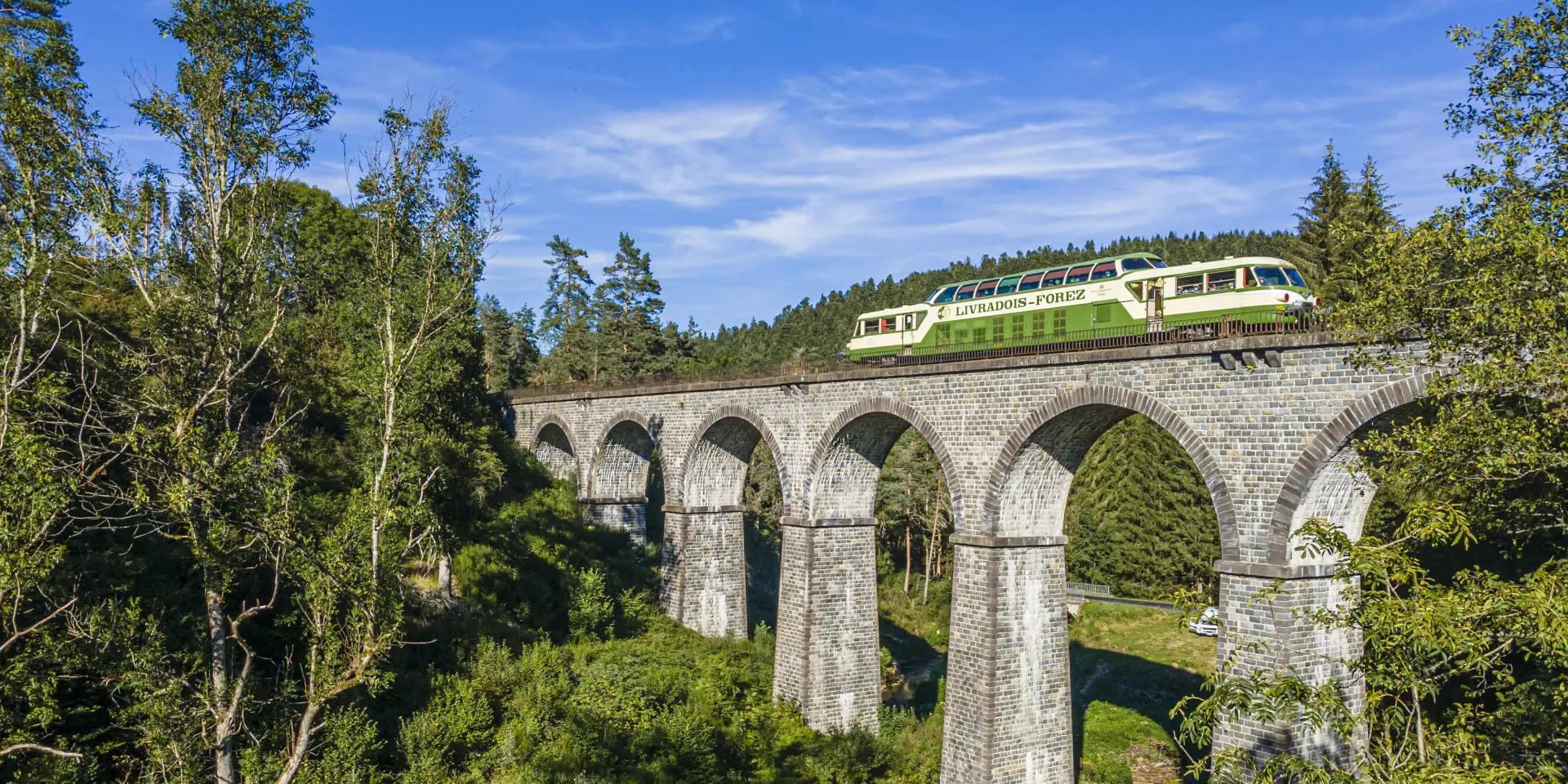 Le train touristique d’Agrivap traverse un pont en été dans les paysages du Livradois-Forez.